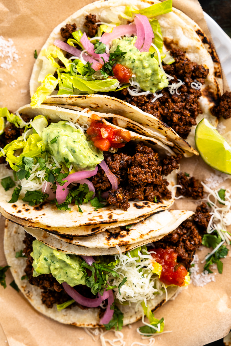 three ground venison tacos on a plate with topped with taco fixings