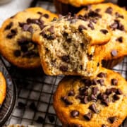 Muffin with one bite taken on a cooling rack with more muffins and a bowl of butter.