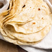 Sourdough tortillas stacked and folded in half on a towel over a cutting board.