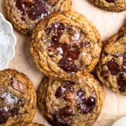 Cookies laid out on parchment paper and sprinkled with flakey sea salt. Sitting next to a pinch bowl of flakey sea salt and a glass of milk.