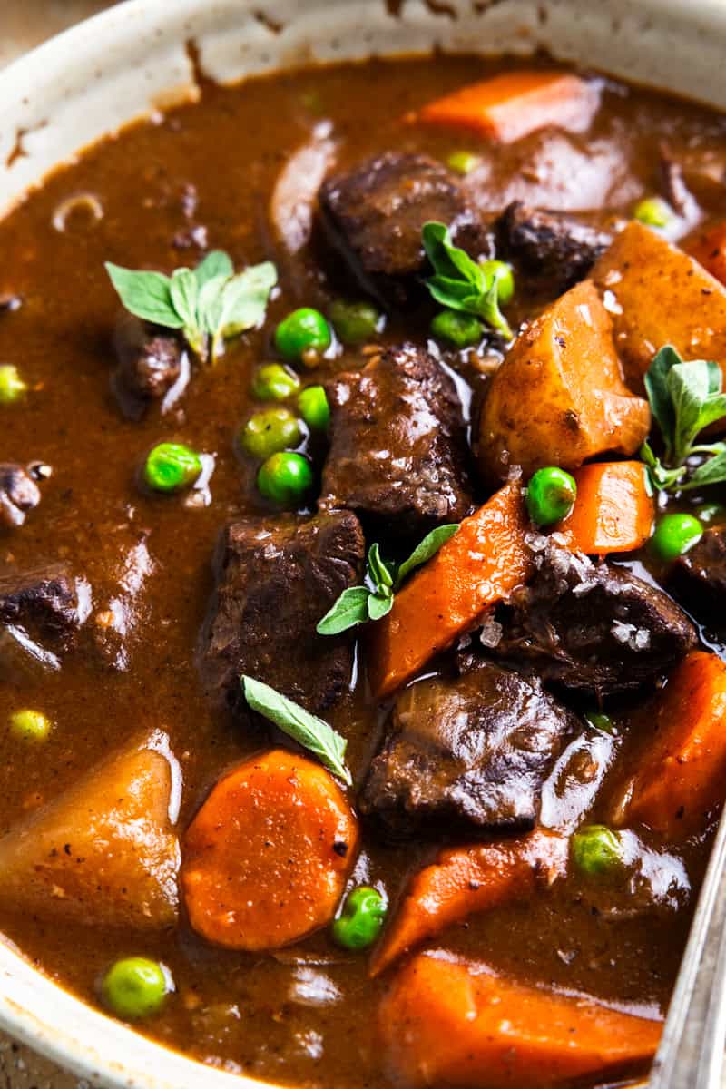 Stew in a bowl with chunks of venison, potatoes, carrots and peas.