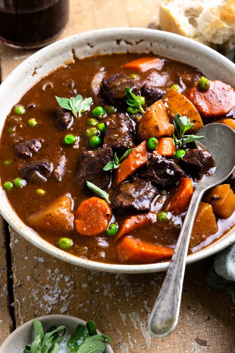Bowl of venison next to a glass of red wine and a piece of bread.