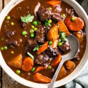 Bowl of venison stew next to a glass of red wine and piece of crusty bread.