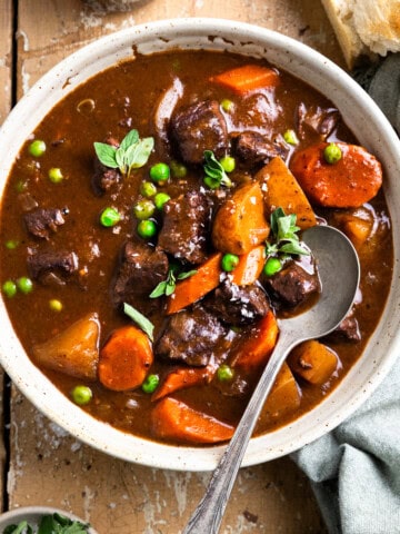 Bowl of venison stew next to a glass of red wine and piece of crusty bread.