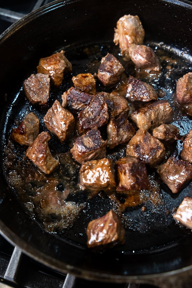 Small chunks of seared venison in a cast iron skillet on the stove top.