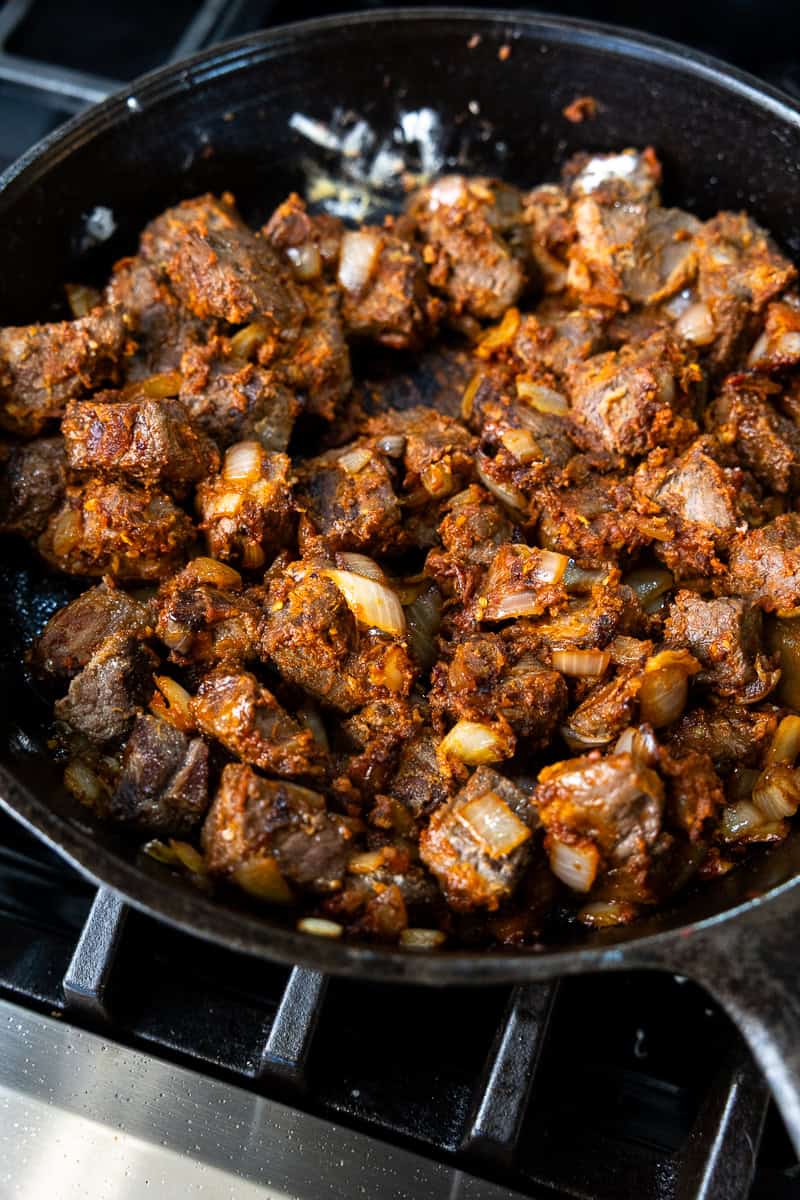 Cast iron skillet on the stove filled chunks of seared venison and sautéed onion mixed with tomato paste and flour.