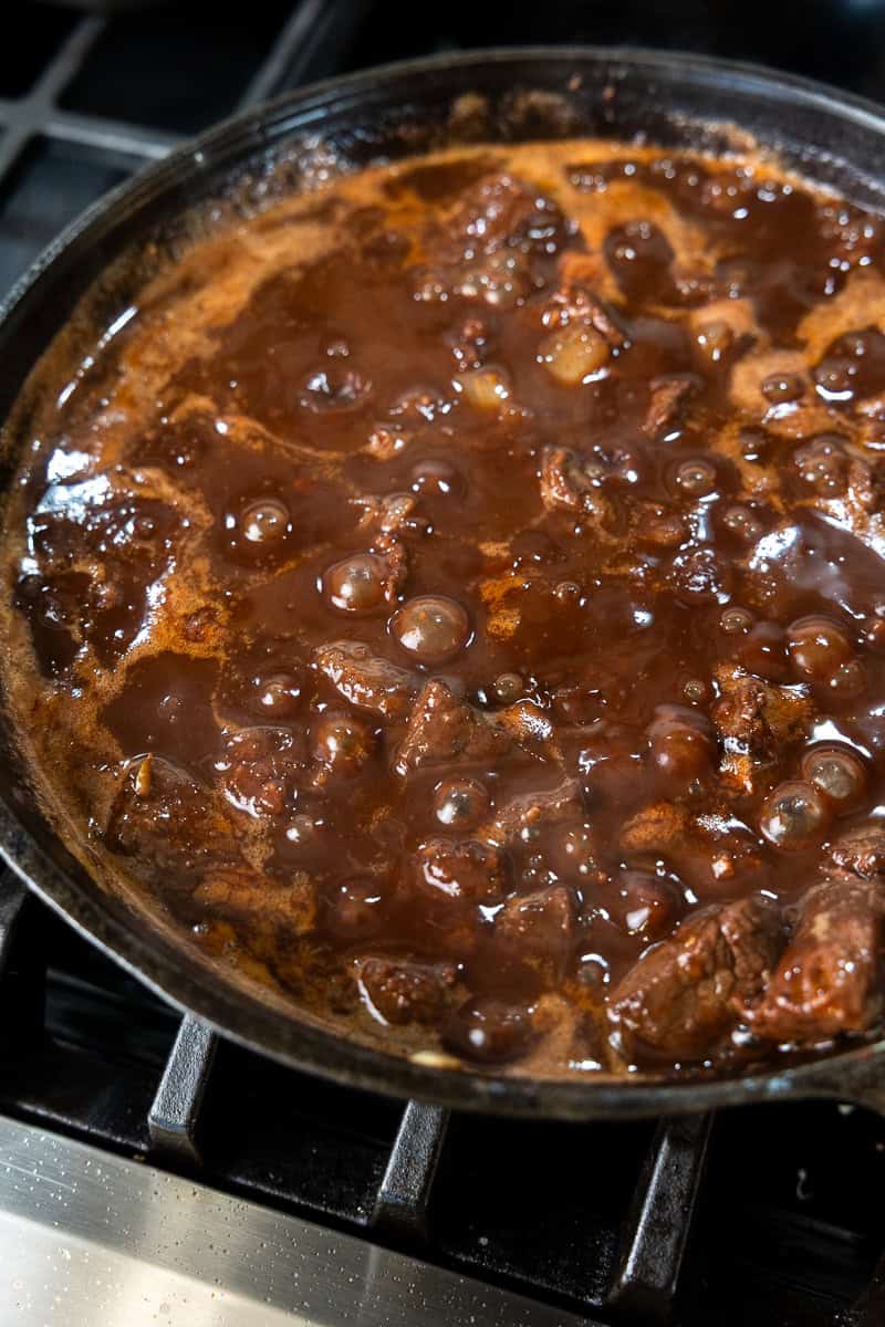 Venison, onion and red wine bubbling on the stove in a skillet.