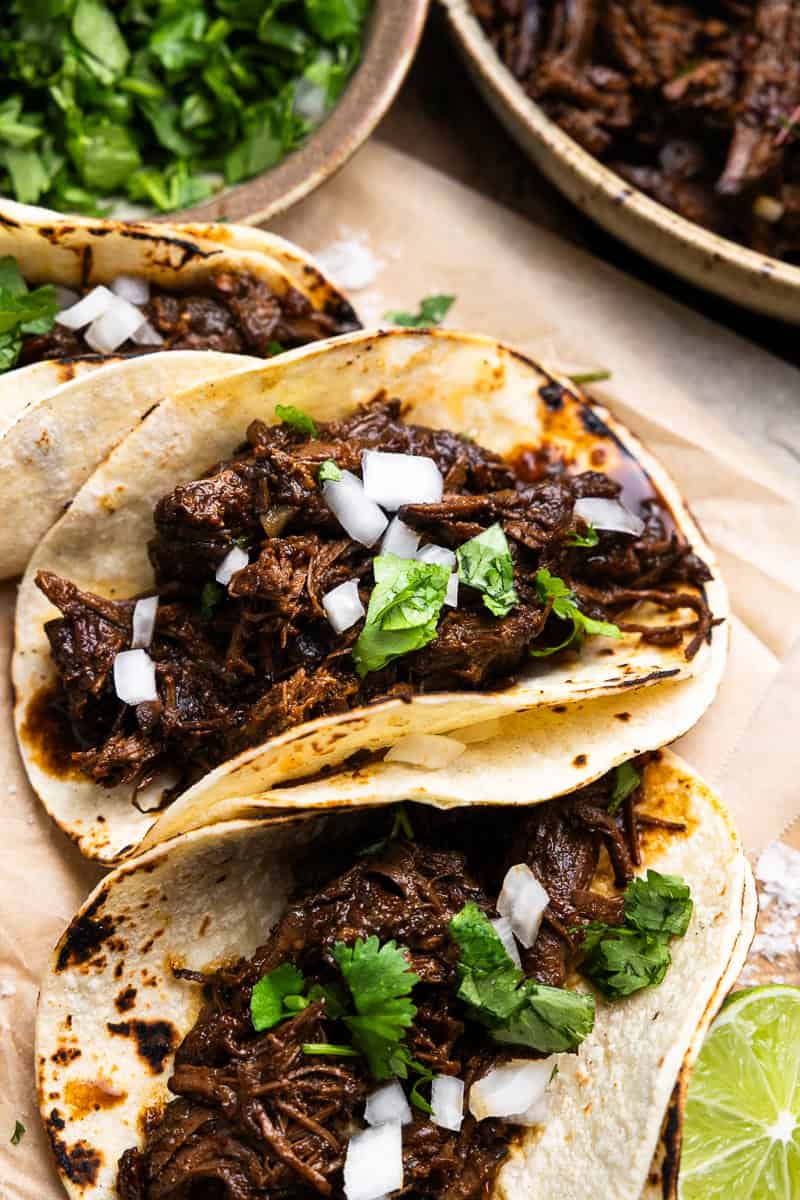 Three venison barbacoa tacos on a cutting board with limes.
