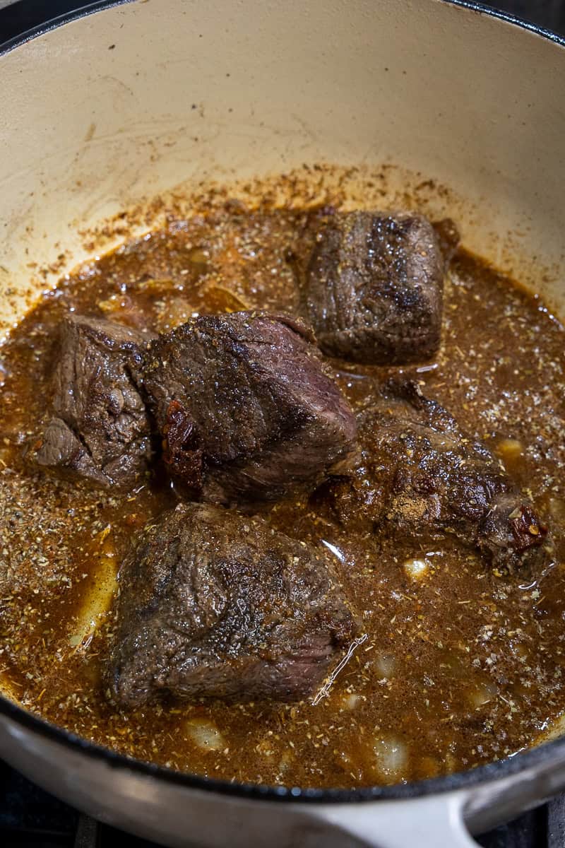 All ingredients to make barbacoa, including hunks of venison roast, in a dutch oven.