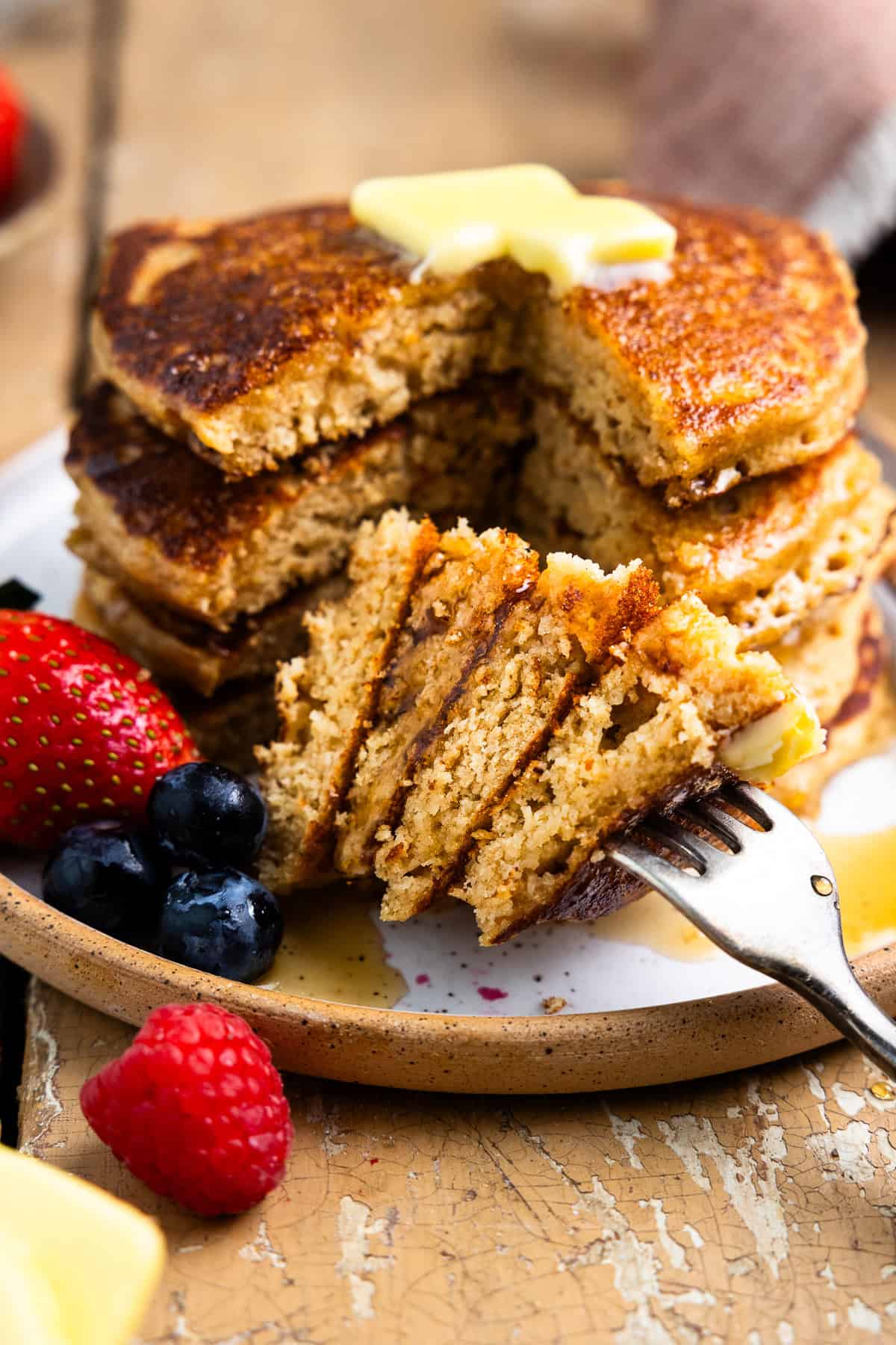 Stack of fresh milled pancakes on a plate with one bite cut out and poked with a fork.