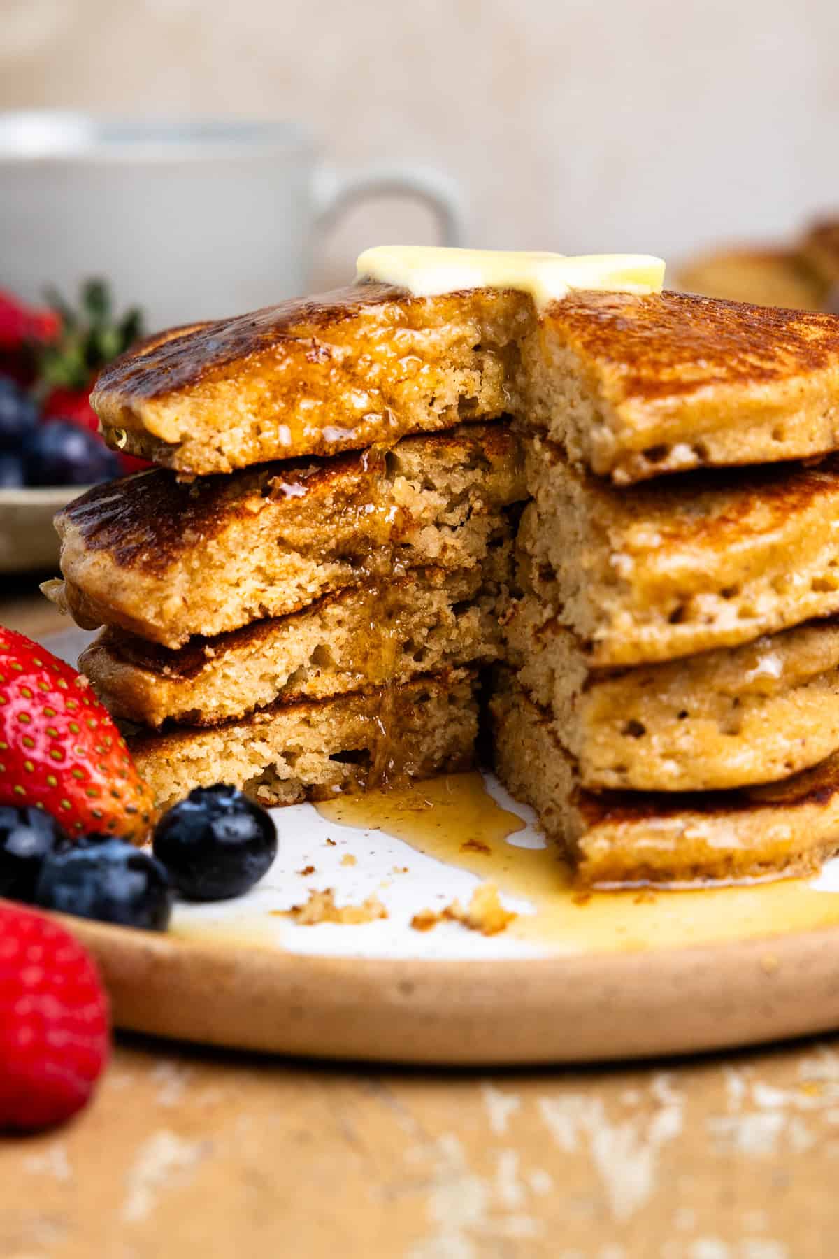 Four fresh milled pancakes on a plate, drizzled with maple syrup and cut into showing the center.