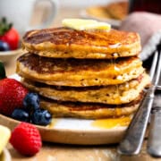 Stack of fresh milled flour pancakes and fresh berries on a plate and drizzled with maple syrup.
