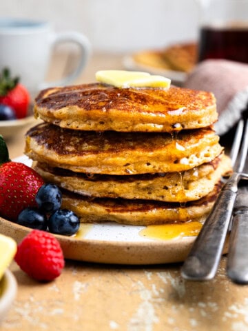 Stack of fresh milled flour pancakes and fresh berries on a plate and drizzled with maple syrup.