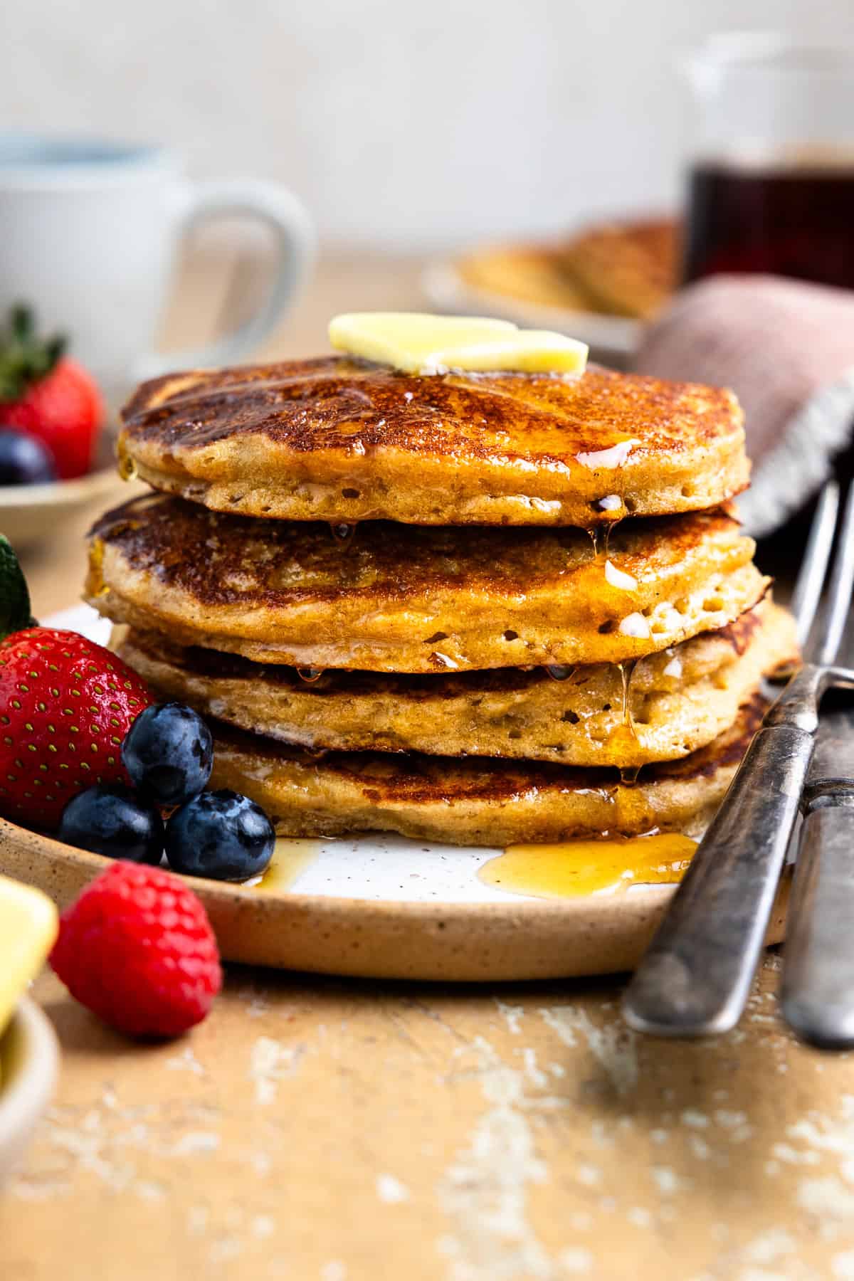 Stack of fresh milled flour pancakes and fresh berries on a plate and drizzled with maple syrup.