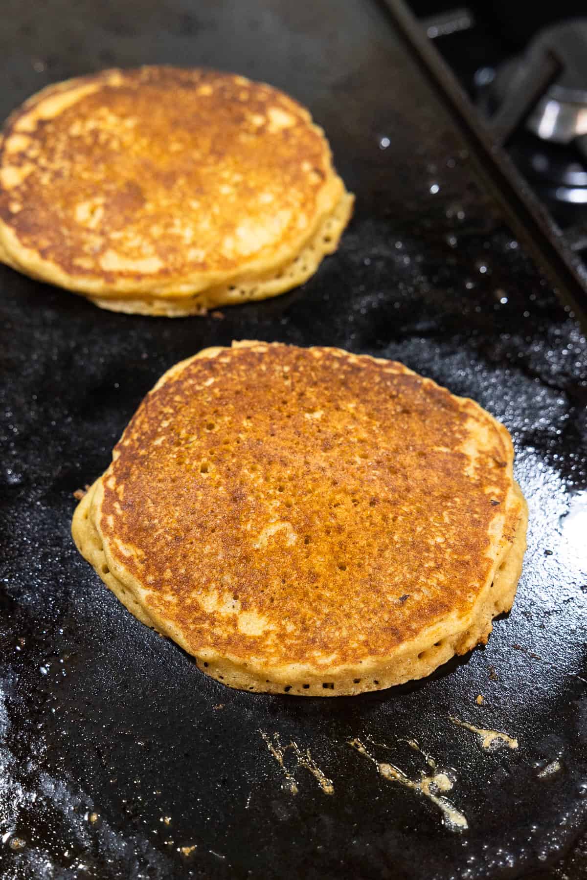 Two pancakes cooking on a griddle.