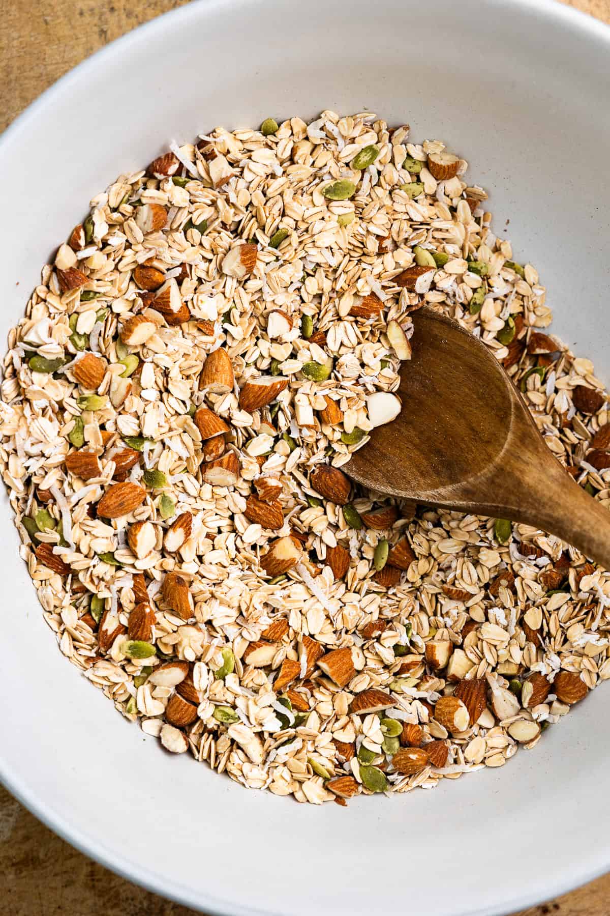 Oats, nuts, pumpkin seeds, coconut flakes, flaxseed, hemp hearts, cinnamon and salt mix in a bowl.