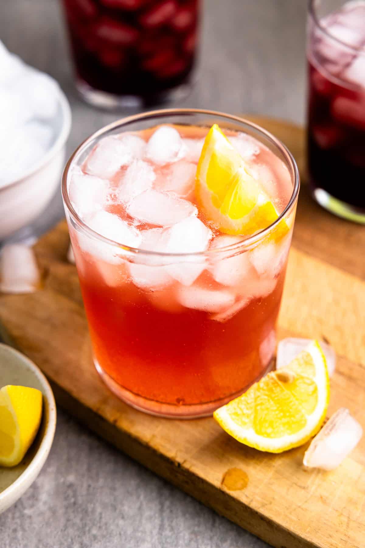 Cranberry pomegranate whey soda in a glass with ice and a lemon wedge next to two glasses filled with grape whey soda.