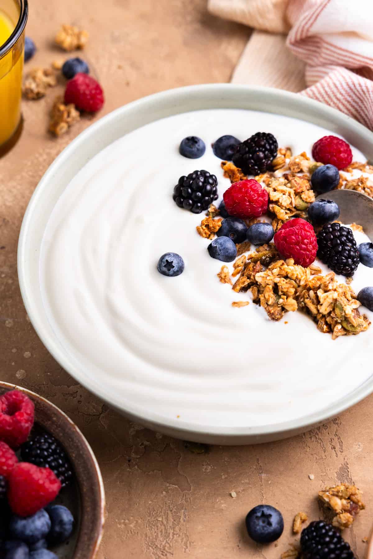 Scooping yogurt in a bowl topped with granola and berries.