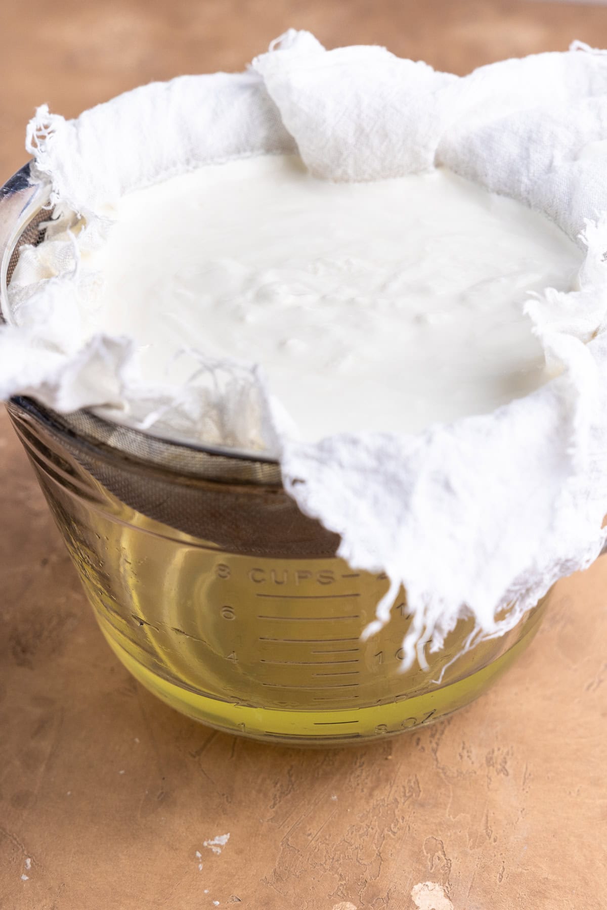 Straining whey from yogurt through a cheesecloth lined mesh strainer into a bowl.