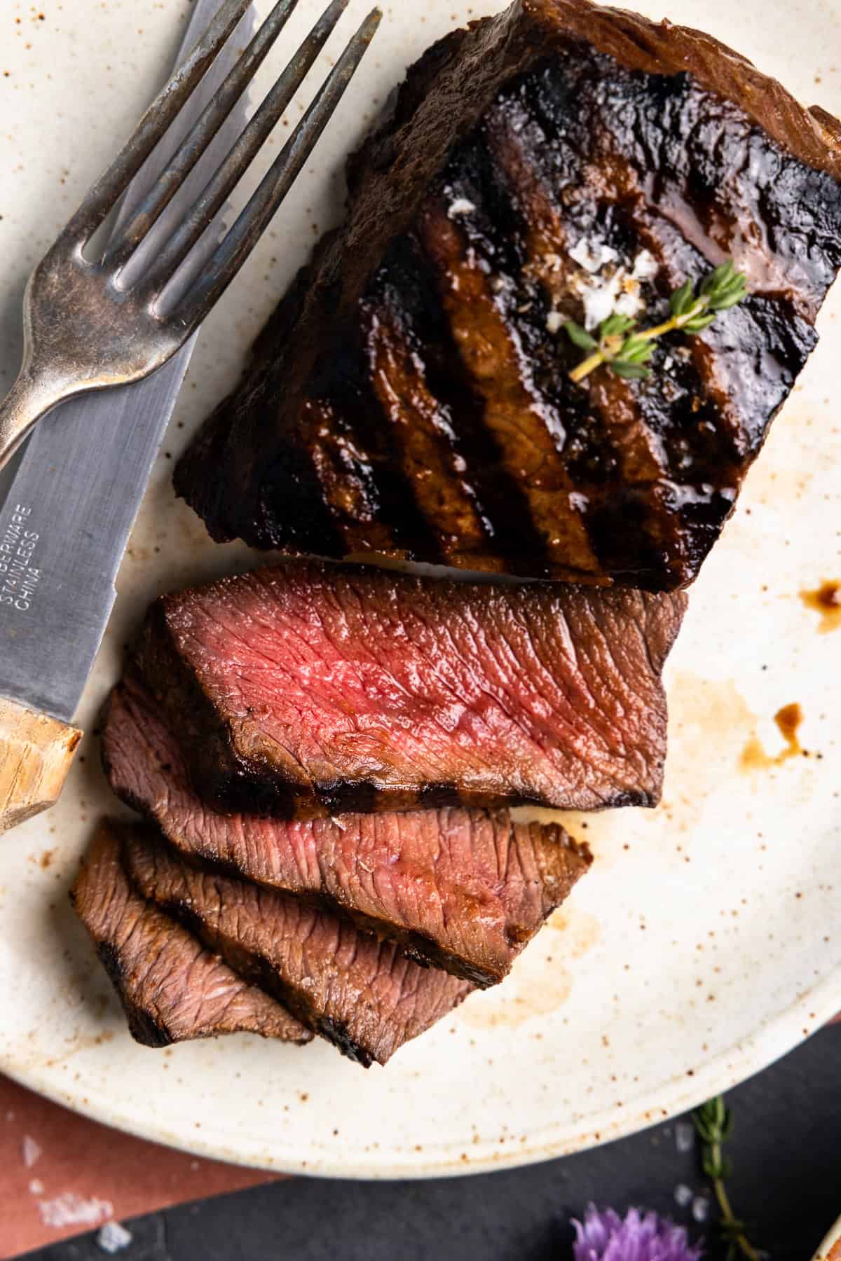 Venison steak sliced on a plate with a knife and fork.
