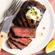 Sliced venison steak on a plate and topped with garlic herb butter.