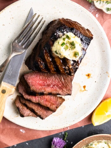 Sliced venison steak on a plate and topped with garlic herb butter.