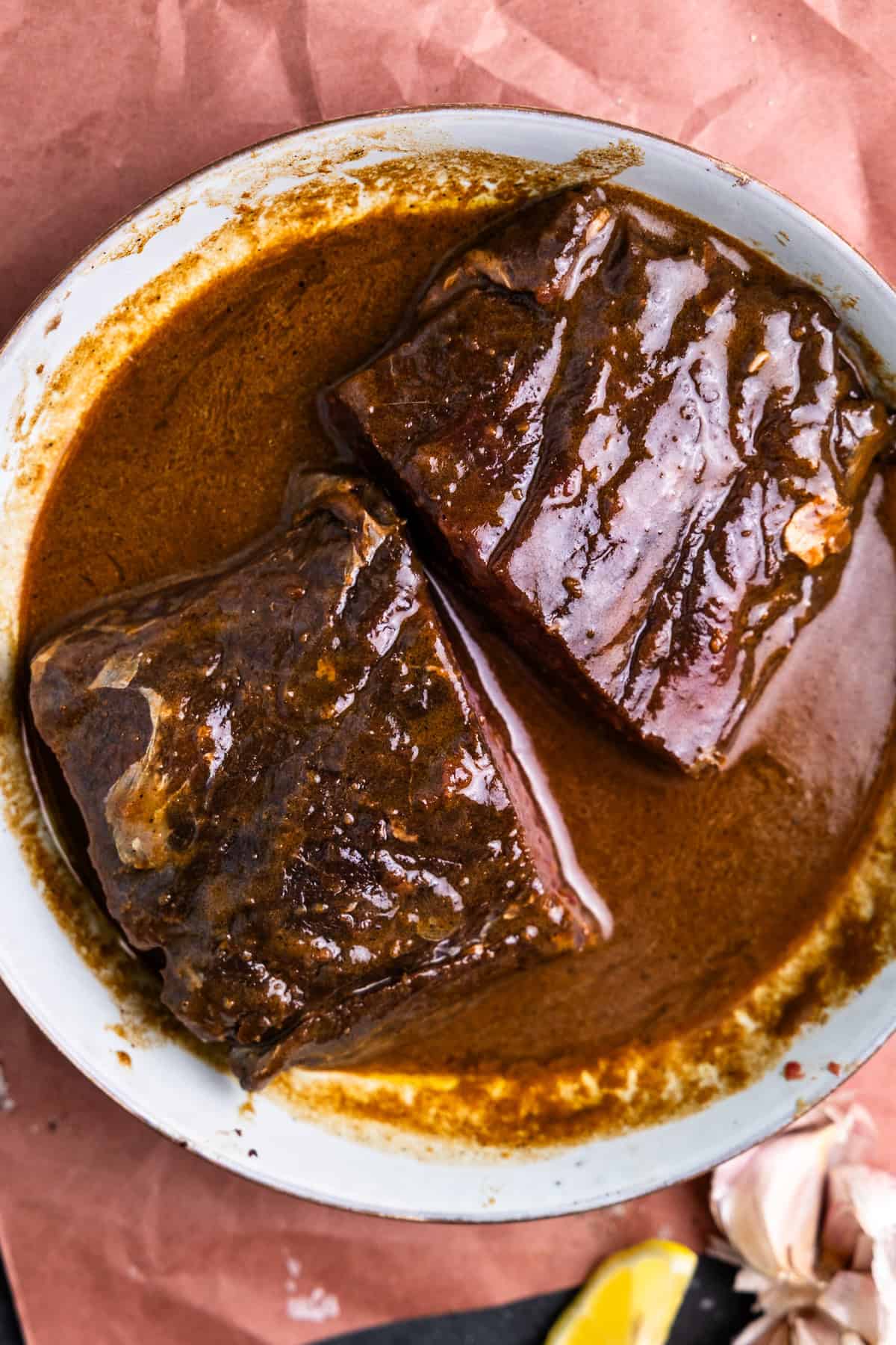 Two venison steaks in a bowl with venison marinade.