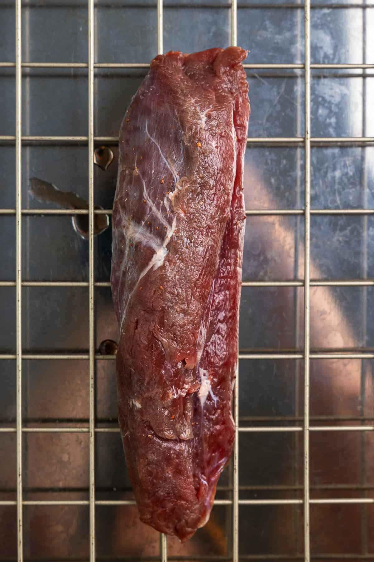 Salt brined venison tenderloin on a wire rack over a sheet pan.