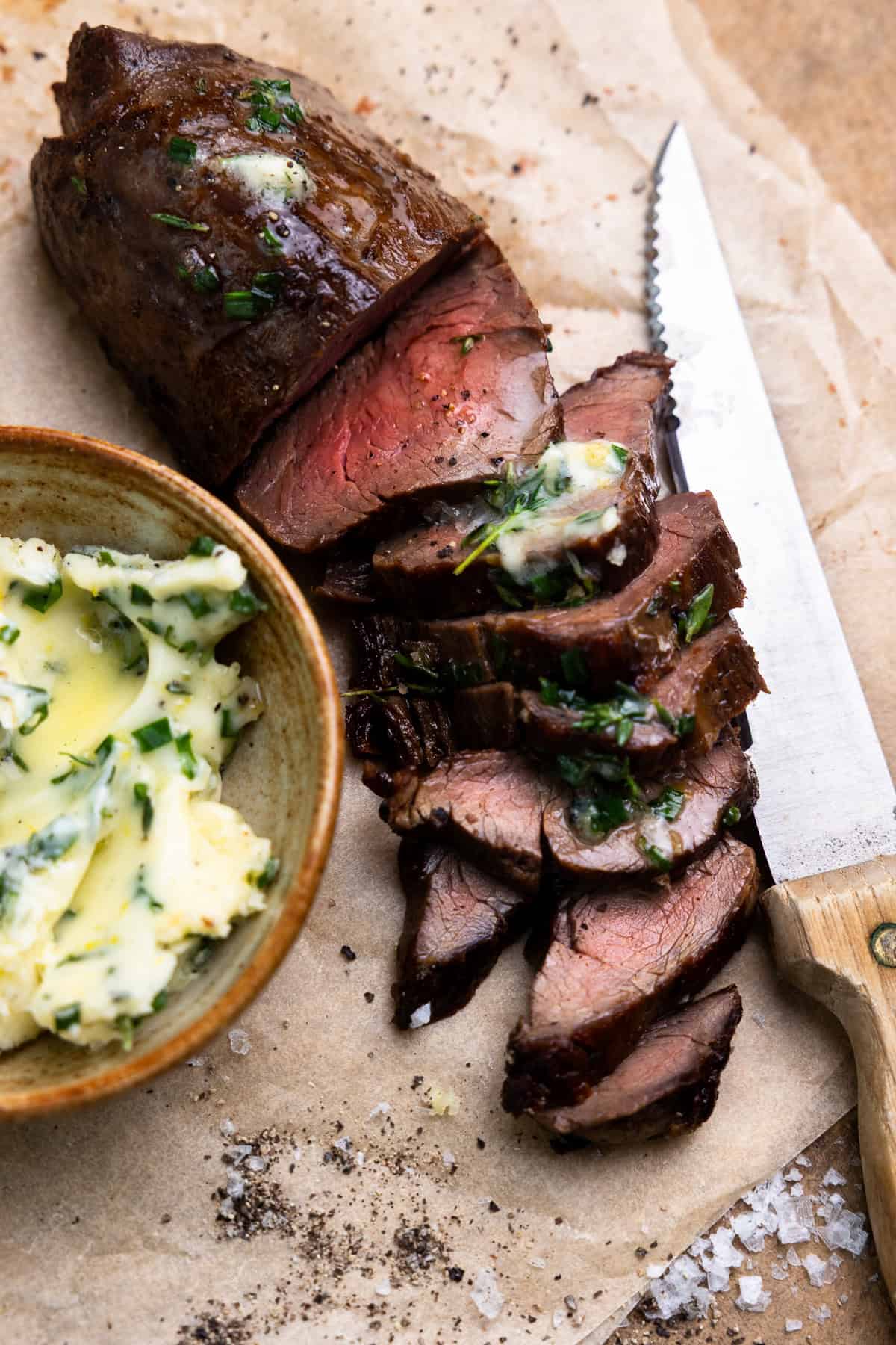 Salt brined and pan-seared venison tenderloin on a cutting board, cut into slices and topped with herb butter.