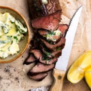 Venison tenderloin sliced on a cutting board and topped with herb butter.
