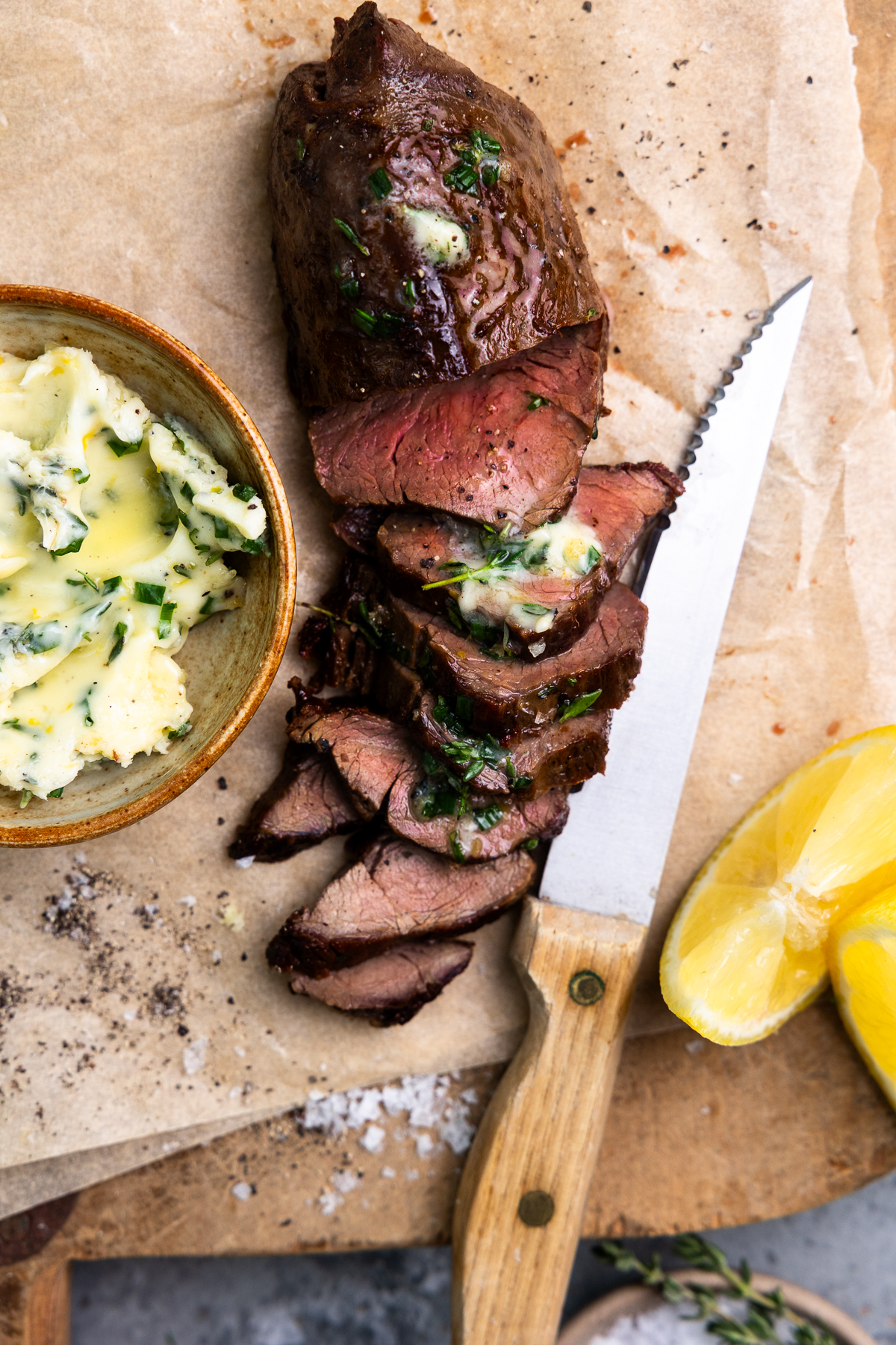 Venison tenderloin sliced on a cutting board and topped with herb butter.