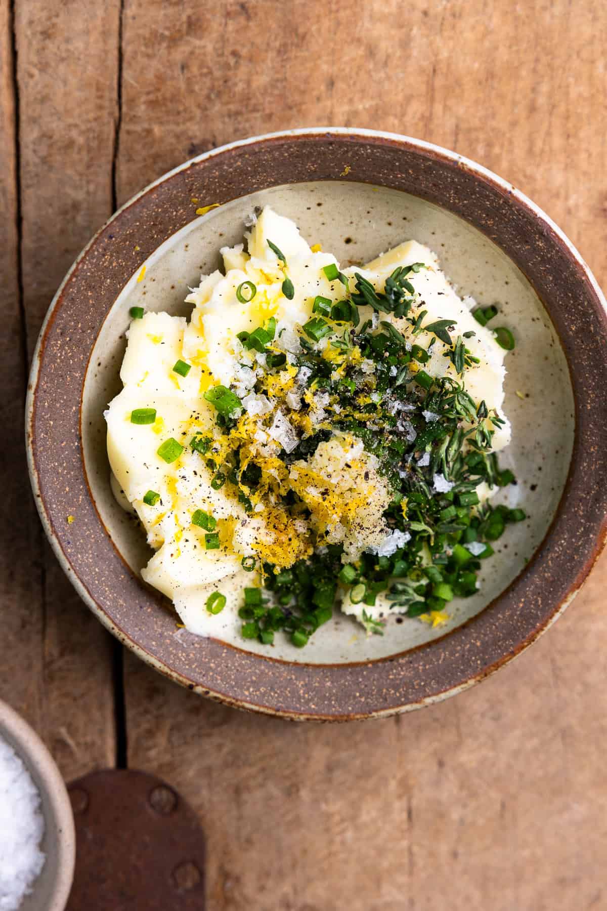 Softened butter in a small dish with fresh thyme, chives, garlic, lemon zest, and salt.